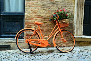 old bicycle with flowers in the basket in front of a brick wall
