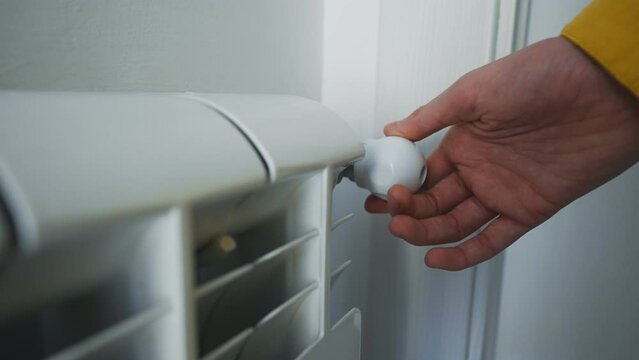 Female hand adjusting thermostat to turn on the radiator heater at home.
