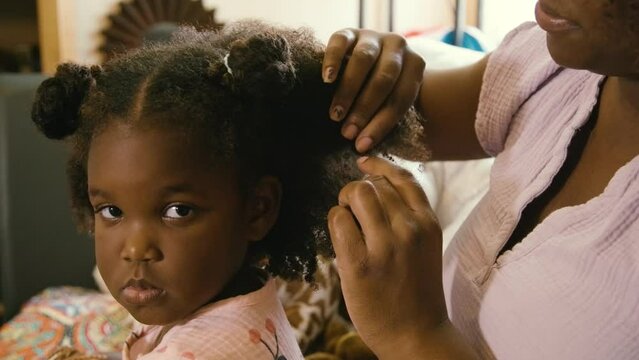 Millennial Black mom caring for her Black daughters and brushing the Black girls' natural curly hair at home