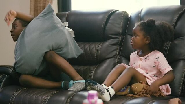 Young Black brother and sister laying down on couch in living room watching television tv as children
