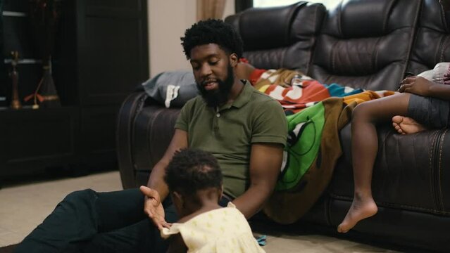 Black millennial father caring for crying infant daughter in living room