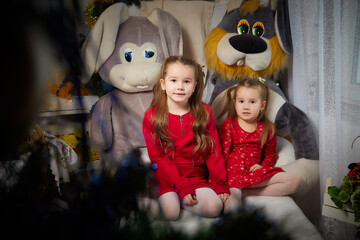 Portrait of a little pretty girls with long beautiful hair in red dress in the room decorated for Christmas with garland lights and dark background. Christmas and New Year holiday