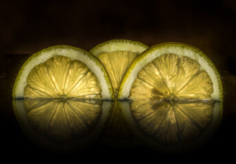 three halves of yellow lemon slices in front of a black background, they are lit behind