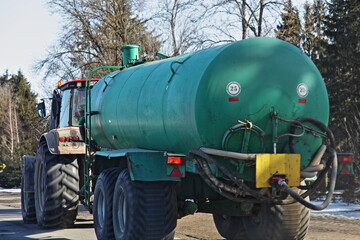 Green sewerage tractor barrel trailer drive on countryside asphalted road at spring day. Sanitation service on countryside