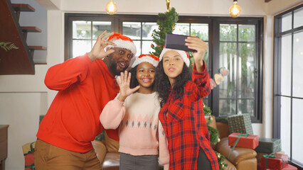 An African American black family, woman, father, mother and kid girl taking a selfie by phone in party on Merry Christmas Eve Xmas on holiday. Celebration at home. People lifestyle.