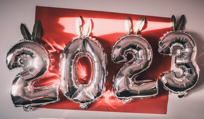 New Year's image with numbers from balls 2023 on a red background and rabbit ears for decoration selective focus