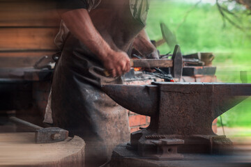 Hands of a man with a hammer on the background of an authentic retro forge. Forging an arrowhead. Added motion blur effect for cinematic look.