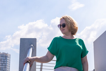 Portrait of a smiling happy middle-aged woman in sunglasses, green blouse standing on the river...