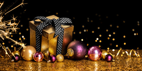 Merry Christmas and Happy New Year! Gift in a golden box with a bow and Christmas balls on a golden...
