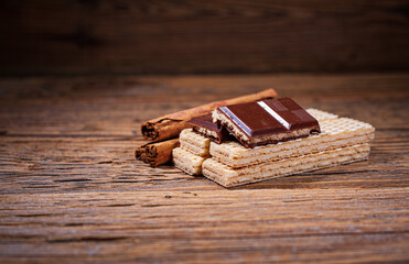 Chocolate, wafers and cinnamon sticks on a wooden background