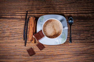 Cup of black coffee with chocolate, cinnamon sticks and vanilla sticks on a wooden background as a...