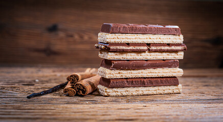 Chocolate, wafers, cinnamon sticks and vanilla stick on a wooden background