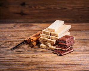 Chocolate, wafers, cinnamon sticks and vanilla stick on a wooden background