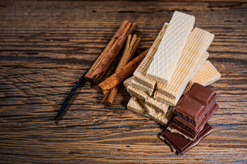 Chocolate, wafers, cinnamon sticks and vanilla on a wooden background