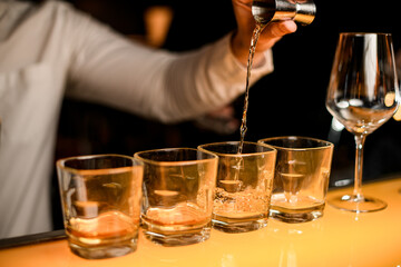 close-up glasses stand on bar and hand of bartender pours drink from jigger into glass