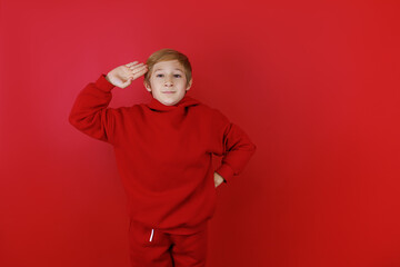 Fototapeta premium on a red background stands a boy dressed in a red suit who put his hand to his head