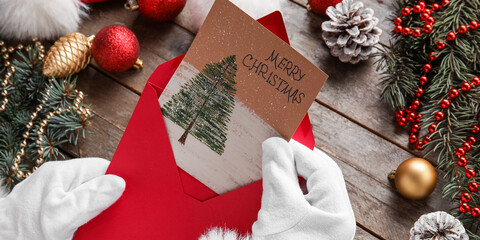 Santa Claus holding envelope with greeting for Merry Christmas at table