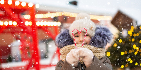 Pretty girl holds in his hands candy cane in the shape of a heart outdoor in warm clothes in winter...