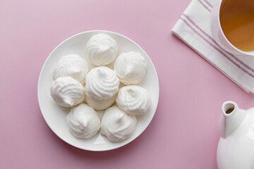 White marshmallows on a white plate on a pink background
