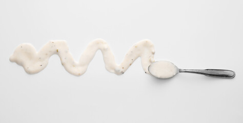 Spoon with tasty spilled Caesar salad dressing on light background