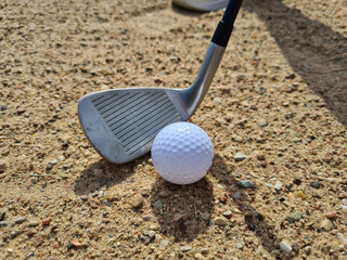 Golf ball trapped with a wedge of sand about to hit golf ball