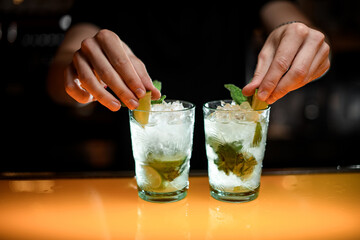 hands of male bartender decorate with green mint leaves glasses with cold mojito