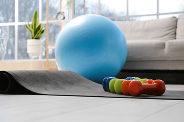 Different dumbbells on yoga mat in room