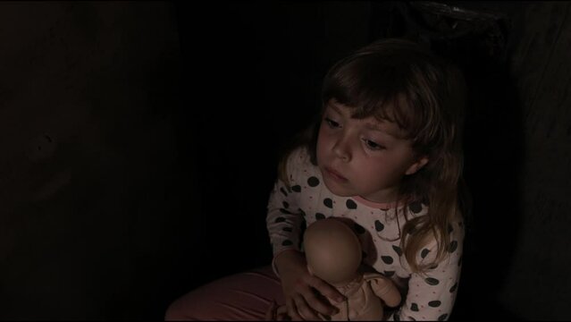 Scared girl with a doll in a dark room