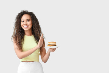 Young African-American woman refusing from burger on light background. Diet concept