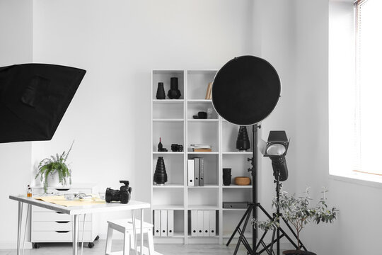 Interior of light office with photographer's workplace, shelving unit and equipment