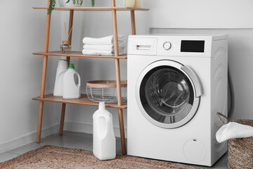 Shelving unit with towels, detergent and washing machine near light wall