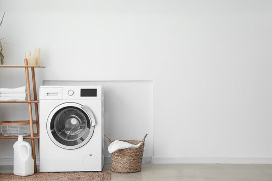 Interior of light laundry room with washing machine, basket and shelving unit