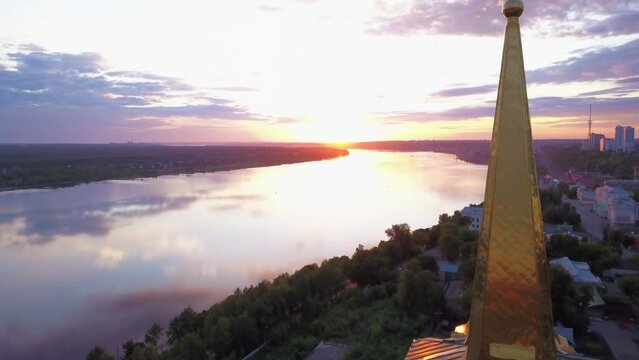 Aerial view of the sunset sky above the wide river. Clip. Green town located along the river.