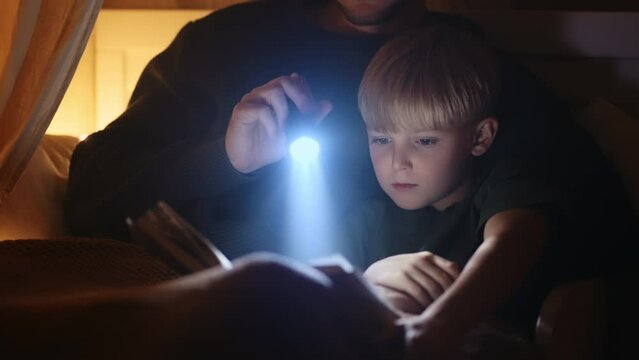 a father lying in bed with his son reads him a fairy tale before going to bed with a lantern. read a book with my son, a lullaby. Father and son in bed. Children's room, to fall asleep, to put to bed