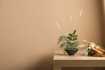 Pot with beautiful ikebana, tree bark and scissors on table near beige wall