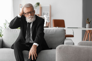 Thoughtful mature man sitting on sofa in office