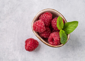 Juicy forest raspberry with mint leaf i a bowl on a light textured background. Healthy food concept.