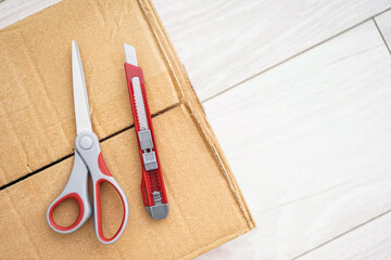 Utility knife with scissors on cardboard box, closeup