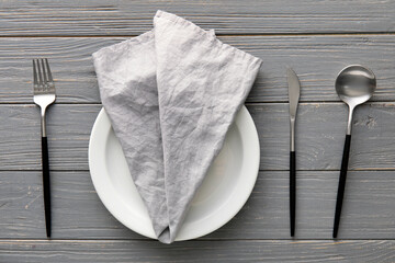 Table setting with napkin in plate and cutlery on grey wooden background