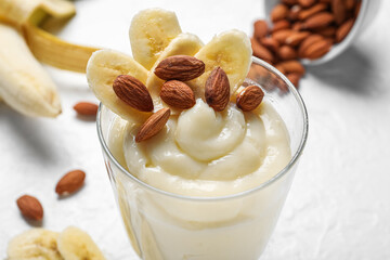 Glass of tasty vanilla pudding with banana and almond nuts on light background, closeup