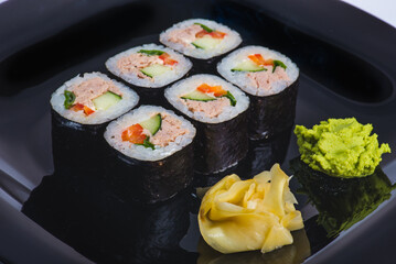 appetizing sushi roll with tuna salmon escolar crab and avocado on a black stone plate.