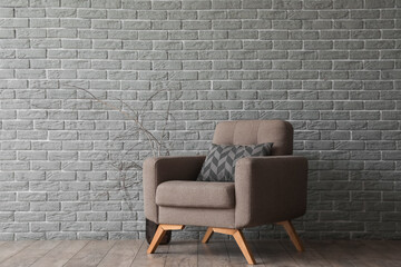 Soft armchair with cushion and tree branches near grey brick wall