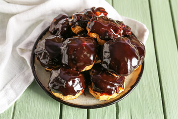 Plate with delicious eclairs on color wooden background