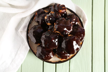 Plate with delicious eclairs on color wooden background