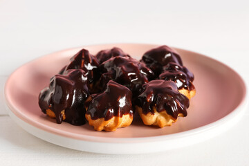 Plate with tasty eclairs on light wooden table, closeup