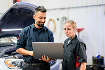 Two Handsome mechanic worker in uniform working on car with laptop