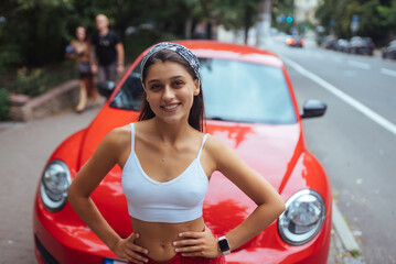 Portrait of pretty Caucasian woman standing against new red car