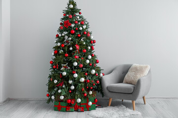 Christmas tree with presents and armchair near light wall