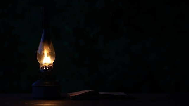 Old antique burning kerosene lamp with open book on the wooden table, close up, copy space