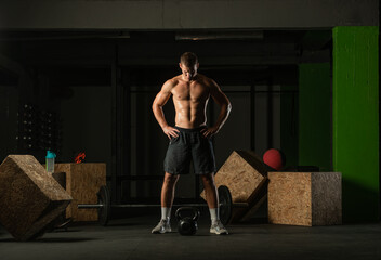 Full-length photo of a handsome man with a naked torso exercising with a kettlebell on a dark...